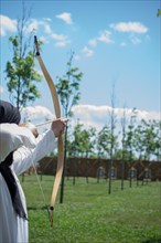 Archer with bow in traditional clothes shooting an arrow
