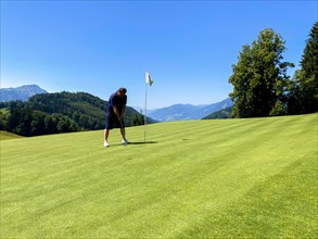 Golfer on Infinity Putting Green with Mountain View in a Sunny Summer Day in Burgenstock