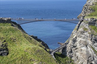 Tourists walk across the new footbridge to the peninsula with the castle ruins of Tintagel Castle