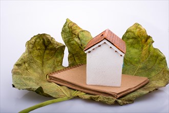 Little model house placed on an Autumn leaf and a brown notebook