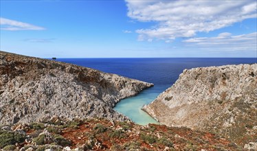 Beautiful view of z-shaped lagoon in typical hills of Crete landscape. Clear blue sky and beautiful clouds on sunny day. Azure sea waters. Red soil in foreground. Stefanou beach
