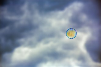 Single soap bubble floating in front of dark cloudy sky