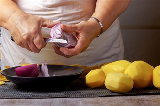 Close-up of a woman's hands in a white apron peeling red onion with a knife