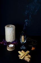 Burning palo santo in a glass cup accompanied by white lighted candles and a Tibetan mala