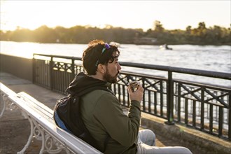 Latin man enjoying the sunset at the river while drinking mate