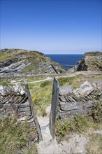 A footpath leads through a stone wall of slates to the Tintagel peninsula and the castle ruins of Tintagel Castle