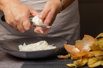 Close-up of a woman's hands in a white apron peeling onion with a knife