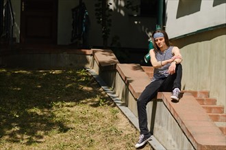 Creative long-haired man in tank top and jeans sits on railing