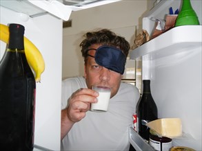 Tired Man with Sleep Mask Drinking Milk in the Refrigerator
