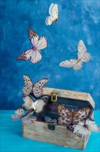 Butterflies flying out of an antique wooden chest against a blue background