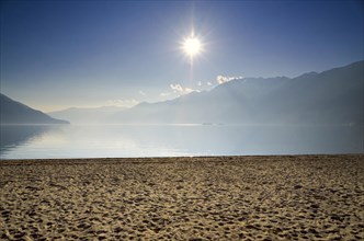 Sand Beach on a Misty Alpine Lake Maggiore with Mountain and Sunlight in Ascona