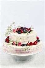 Summery fresh two tier wedding cake decorated with berries and flowers festive cream cake on light background
