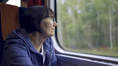 Elderly lady in glasses travels in train and looking out the window