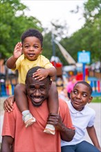 Portrait of African black ethnicity father smiling with his children at playground in city park