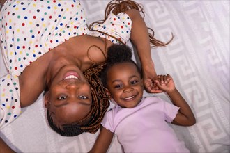 Black African ethnicity family mother with daughter in bedroom on bed smiling