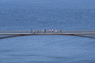 Tourists walk across the new footbridge to the peninsula with the castle ruins of Tintagel Castle