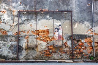 Street art brother and sister on a swing on a wall in George Town on Penang Island