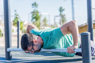 Man seen in profile with beard and sunglasses doing push-ups on a bar on the floor