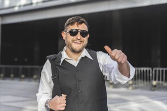 Portrait of a smiling businessman looking at the camera with his thumb up outside his office