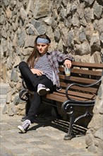 Long haired man sitting on bench with glass of drink in a sunny day