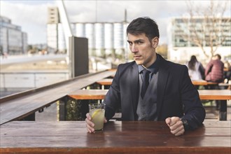 Businessman sitting at an outdoor bar drinking lemonade looking at the camera