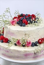 A two tier wedding cake decorated with berries and flowers festive cream cake on a light background