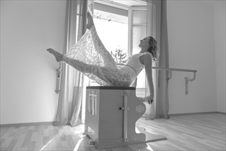 Woman Exercising on Pilates Machine Against a Window With Sunlight