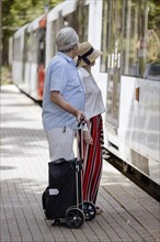 Elderly couple waiting with a trolley at a stop for the tram