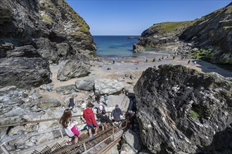 Tourists descend between rock cliffs on a staircase to Tintagel Haven