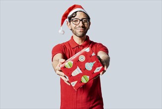 Smiling guy in christmas hat offering you a christmas gift box. Christmas man offering a gift boxes isolated. Handsome man in christmas clothes showing a gift box