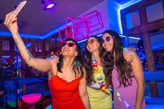 Friends at a nightclub taking a selfie at a night party on summer vacation in a pub