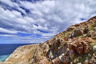 Beautiful wild red cliffs against clear blue sky and dynamic clouds. Diagonal compositition. Typical Greek or Cretan landscape. Mediterranean islands. Diagonal hills. Blue sea waters