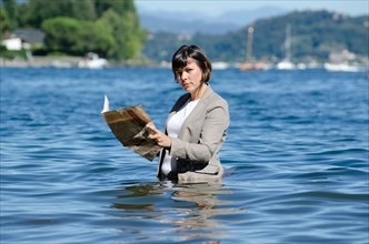 Elegant Business Woman with Suit Standing in the Water and Reading a Newspaper