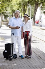 Elderly couple waiting for the tram at a stop with a smartphone in hand