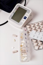 Daily pill box with blood pressure monitor in the background isolated on a white background