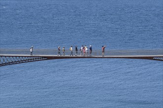 Tourists walk across the new footbridge to the peninsula with the castle ruins of Tintagel Castle