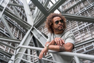 Young man with afro hair wearing sunglasses on the stairs in the city