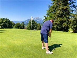 Golfer on Putting Green with Mountain and the Moon View in a Sunny Summer Day in Burgenstock