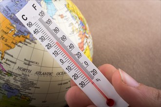 Hand placing a thermometer on a little model globe