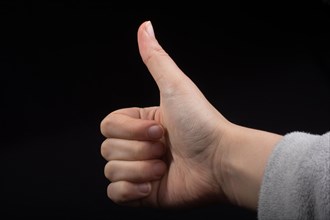 Young hand with thumb up on black background