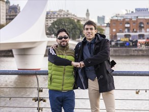Two male friends hugging while looking at camera near Puente de la Mujer