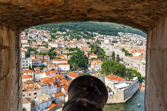 View of the old town through an opening in the wall of the fortress with a cannon in Dubrovnik