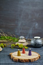 Colorful incense cones on a wooden disk with candles and zen stones stacked on top of them