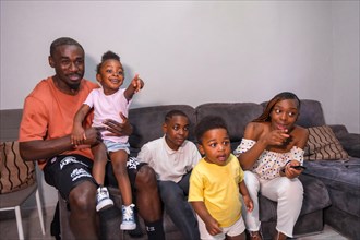 Portrait of black African ethnicity family with children on the sofa at home watching TV