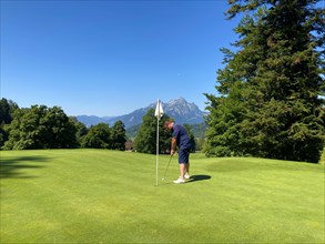 Golfer on Putting Green with Mountain View and the Moon in a Sunny Summer Day in Burgenstock