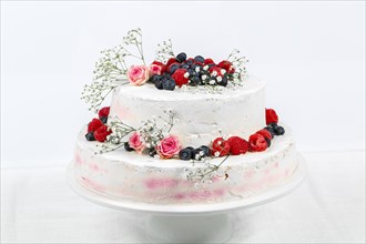 Summery fresh two tier wedding cake decorated with berries and flowers festive cream cake on light background