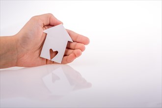 Hand holding a paper house with a heart carved in it on a white background