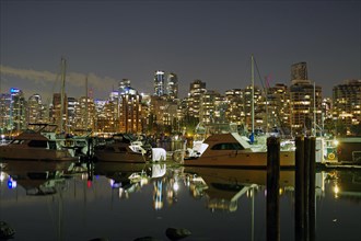 Illuminated skyscrapers and pleasure boats reflected in the calm water