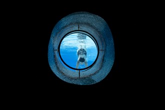 Woman Swimming in the Ship Porthole in Underwater in Swimming Pool in a Sunny Day in Switzerland