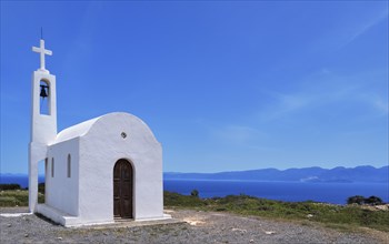 White Greek Orthodox chapel or church on hilltop of seashore against clear blue sky on sunny day. Traditional religious building. Typical Greek landscape. Diagonal composition